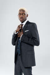 blonde african american man in formal wear adjusting tie isolated on grey