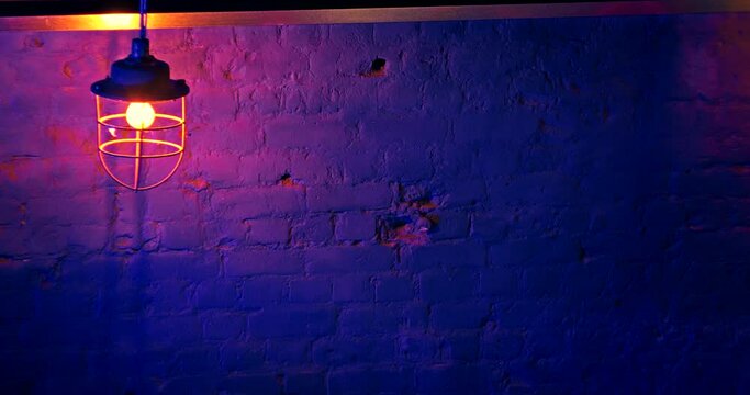Old style iron loft lantern with yellow electric bulb against blue brick wall in nightclub. Neon lighting in the club. Nightclub interior design. Shadows on the brick wall of the club.