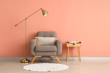 Wooden table, soft armchair and standing lamp near pink wall