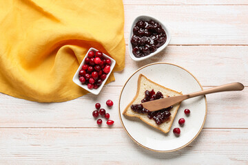 Spreading tasty lingonberry jam on toast with knife on light wooden background