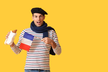 Surprised young man with flag of France and croissants on yellow background
