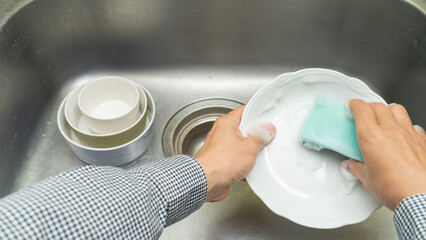 洗剤をつけたスポンジで食器を洗う