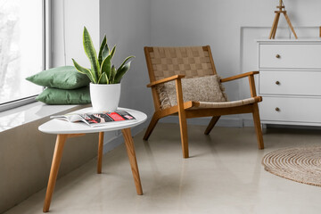 Modern table with houseplant, magazine and chair in interior of room