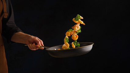 Chef roasts shrimp with vegetables on black background .freezing in motion.Seafood food.Concept of cooking and gastronomy. Black background for text - 492905490