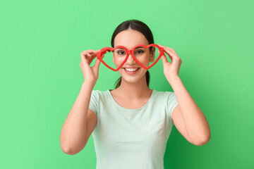 Young woman with funny eyeglasses on green background. April Fools Day celebration