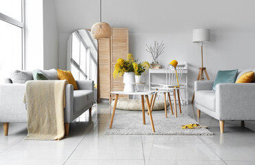 Vase with mimosa flowers on table and sofa in interior of living room
