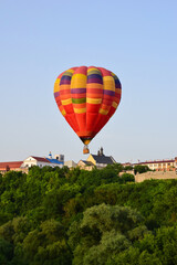 Fototapeta na wymiar A multi-colored inflatable balloon with a gondola flies over the ancient city and the green forest