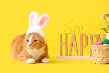 Cute cat in bunny ears, basket, Easter eggs and flowerpot on yellow background