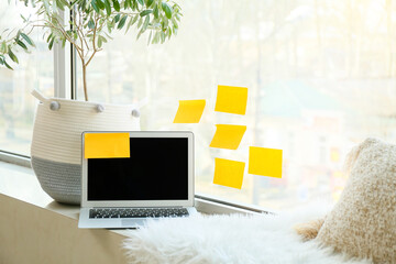 Laptop with sticky notes and houseplant on windowsill