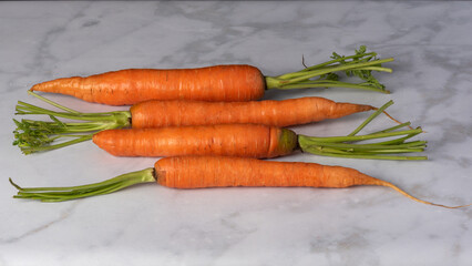 Angle view of organic carrots in parallel on white marble background, with copyspace - healthy eating concept