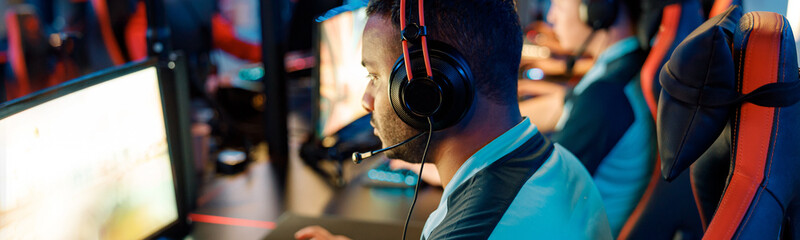 Rear view of cybersport gamer wearing headphones playing online video game while participating in esports tournament in internet cafe © Yaroslav Astakhov