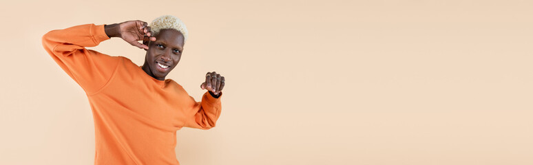 happy african american man in orange sweatshirt looking at camera isolated on beige, banner - Powered by Adobe
