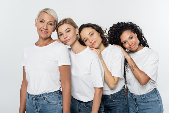 Young multiethnic women in white t-shirts hugging near smiling friend isolated on grey, feminism concept.