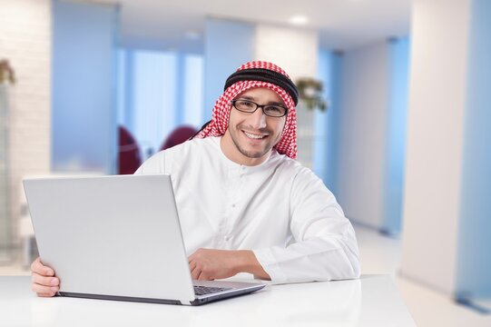 Handsome man with dish dasha working in his business office, successful businessman in traditional emirates white dress.