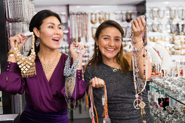 Two cheerful female customers showing variety of stylish necklaces and pendants purchased from costume jewelry salon