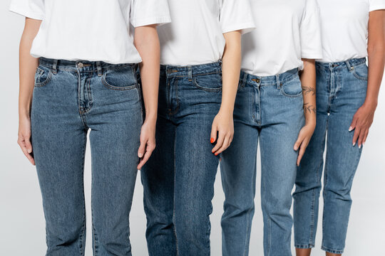 Cropped view of interracial women in jeans and t-shirts isolated on grey.