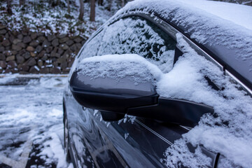 Selective focus on an icy, snow covered car rear view mirror during a snowstorm in the pacific northwest woodlands