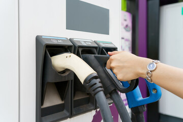 Unrecognizable Asian woman holding a DC - CCS type 2 EV charging connector at EV charging station.
