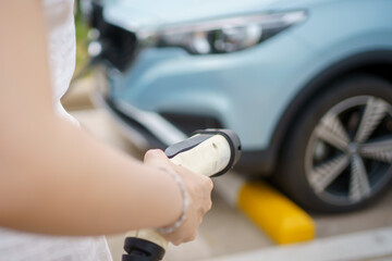Unrecognizable Asian woman holding a DC - CCS type 2 EV charging connector at EV charging station.