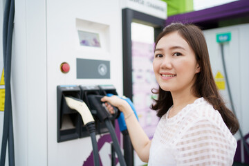Fototapeta na wymiar Unrecognizable Asian woman holding a DC - CCS type 2 EV charging connector at EV charging station.
