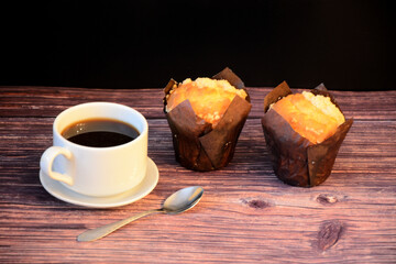 A cup of freshly brewed black coffee and two delicious cupcakes on a wooden table.