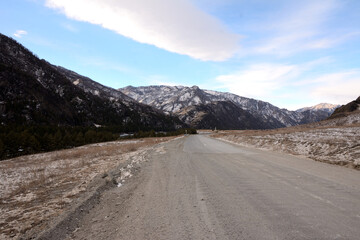 A field road running through a winter valley surrounded by high snow-capped mountains.