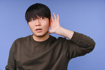 Young asian korean man listening for some secret information news rumors with a hand on ear...