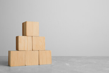 Pyramid of blank wooden cubes on grey table against light background. Space for text