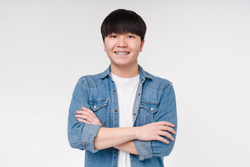 Closeup portrait of a smiling confident asian korean boy man student freelancer in denim shirt looking at the camera with arms crossed isolated on white background.