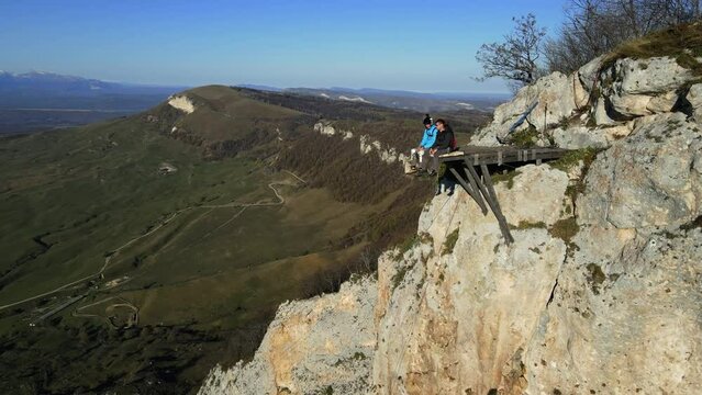two men are sitting on the edge of a cliff and talking, two athletes are preparing to jump with a parachute