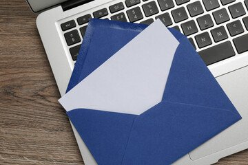 Blue envelope with blank letter and laptop on wooden table, top view