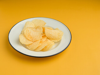 Potato chips or crisps in a white dish on an orange background