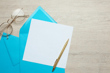 Envelopes with blank paper card, glasses and pen on white wooden table, flat lay. Space for text
