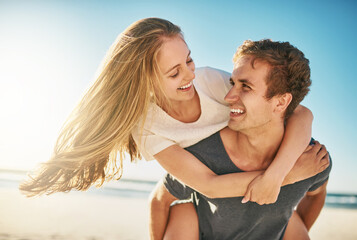 You make this lovely day even more beautiful. Shot of a happy young couple enjoying a piggyback ride at the beach.
