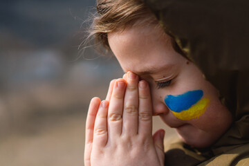 Ukrainian boy closed her eyes and praying to stop the war in Ukraine. Hands folded in prayer...