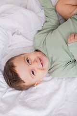 Obraz na płótnie Canvas portrait of a cute smiling baby in a green cotton bodysuit lying on a white bed on his back