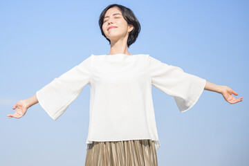 腕を伸ばして深呼吸する女性　青空