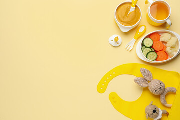 Healthy baby food in bowl and accessories on yellow background, flat lay. Space for text