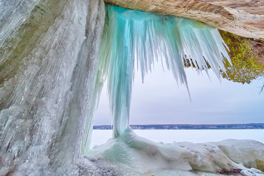Large sharp blue icicles hanging from rocks next to frozen lake in winter