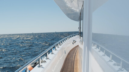 White yacht deck sailing on sea waves on sunny day, close-up. Sea voyage on luxury yacht. Clear blue sky above horizon. Concept of success, travel cruise, lifestyle, freedom. No people
