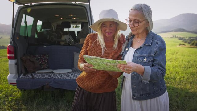 Senior women friends using map outdoors in nature, caravan trip holiday.