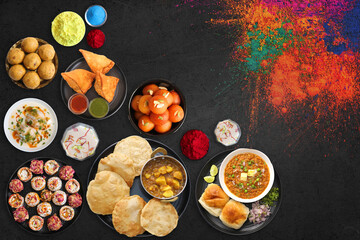 Assorted Indian Holi festival food like samosa, kachori, Puri bhaji, Pav Bhaji, Laddo, Sweets, Dahi vada and Almond milk Thandai drink with colorful background and colors with copy space.