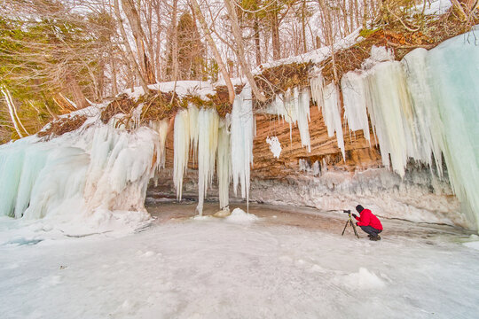 Photographer capturing image of icicles covering cliffs on lake