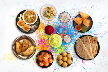 Assorted Indian Holi festival food like samosa, kachori, Puri bhaji, Pav Bhaji, Laddo, Sweets, Dahi vada, puranpoli, gujiya, gulab jamun with colorful background and colors with copy space.