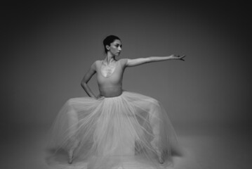 classic black and white portrait, young pretty, fragile, beautiful ballerina dancing in a long pale pink dress with tulle on a uniform background, hand movements, restrained tone. Ballet, dance, dance