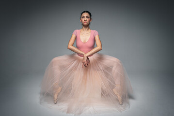 Naklejka premium young pretty, fragile, beautiful ballerina dancing in a long pale pink dress with tulle on a uniform background, hand movements, restrained tone. Ballet, dance, dancer. Place for inscription