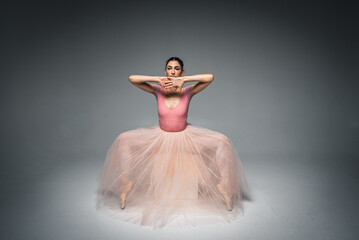 Fototapeta premium young pretty, fragile, beautiful ballerina dancing in a long pale pink dress with tulle on a uniform background, hand movements, restrained tone. Ballet, dance, dancer. Place for inscription