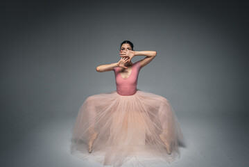 Fototapeta na wymiar young pretty, fragile, beautiful ballerina dancing in a long pale pink dress with tulle on a uniform background, hand movements, restrained tone. Ballet, dance, dancer. Place for inscription