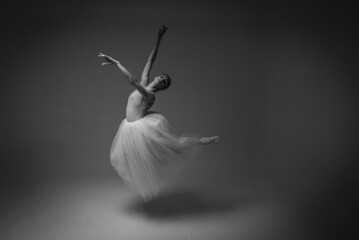 classic black and white photo, young pretty, fragile, beautiful ballerina dancing in a long pale pink dress with tulle on a uniform background, restrained tone. Ballet, dancing, dancer selective focus
