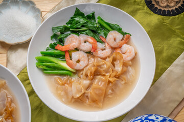 Wide Rice Noodles with Shrimp and kale in Gravy Sauce  Served with condiments, chili powder , chili sauce and sugar. Asian food.